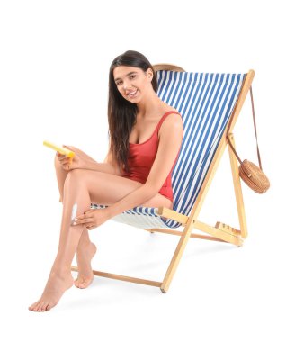 Güzel genç bir kadın beyaz arka planda iskemlede güneş kremi sürüyor.