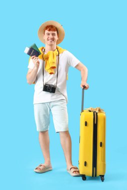 Mavi arka planda pasaportu ve bavulu olan genç bir adam.