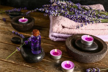 Kaliteli yağ, spa taşları, yanan mumlar ve ahşap masa üzerinde lavanta çiçekleri olan kompozisyon.