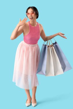 Mavi arka planda alışveriş torbaları olan mutlu, güzel Asyalı kadın.