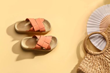 Hasır çantalı kadın tarzı terlikler ve soluk sarı arka planda yelpaze.