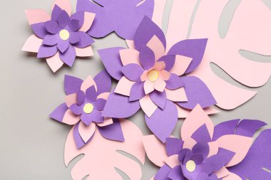 Gri arkaplanda yaprakları olan renkli origami çiçekleri