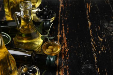 Siyah ahşap zemin üzerinde taze zeytinyağı bulunan farklı cam eşyalar.