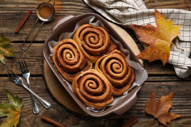 Ahşap zemin üzerinde lezzetli tarçın ruloları ve sonbahar yaprakları pişirme yemeği