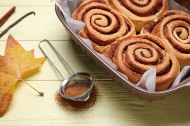 Lezzetli tarçınlı çörekler ve sarı ahşap arka planda sonbahar yaprağı pişirmek.