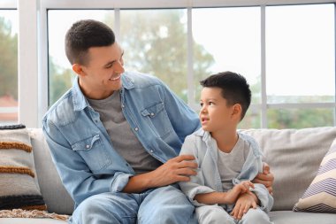 Küçük oğluyla birlikte evdeki kanepede oturan genç adam.