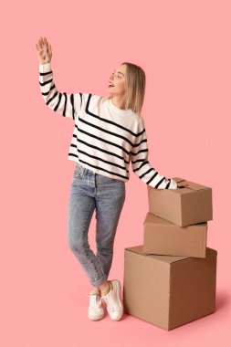Karton kutuları ve pembe arka planı olan mutlu genç bir kadın. Yeni ev konseptine geçiyoruz.