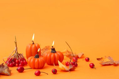 Balkabağı şeklinde yanan mumlarla ve turuncu arka planda sonbahar yapraklarıyla güzel bir kompozisyon.