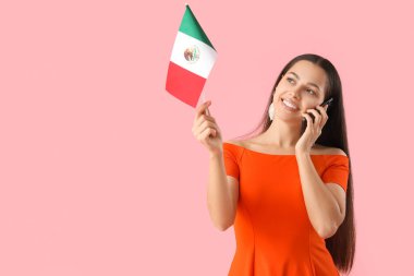 Meksika bayrağı taşıyan genç bir kadın pembe arka planda cep telefonuyla konuşuyor.