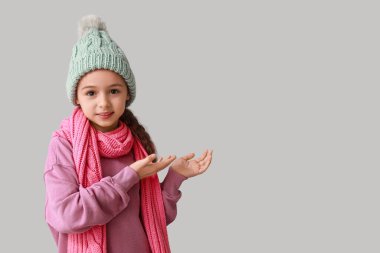 Gri arka planda bir şeyler gösteren kışlık giysili şirin küçük kız.
