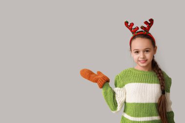 Geyik boynuzları takmış tatlı küçük kız gri arka planda bir şey gösteriyor.