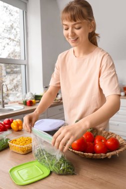 Beautiful young woman with vegetables for freezing in kitchen