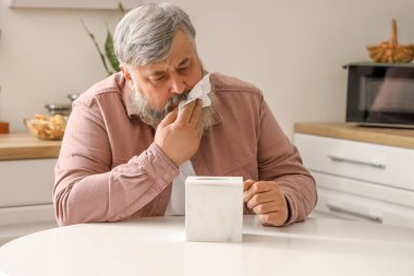 Mutfaktaki masada oturan peçeteli üzgün yaşlı adamın portresi.