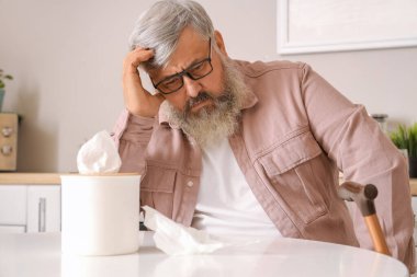 Mutfaktaki masada oturan peçeteli üzgün yaşlı adamın portresi.