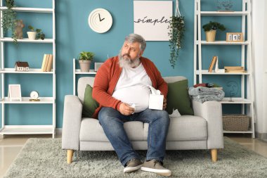 Oturma odasındaki kanepede oturan peçeteli üzgün yaşlı adamın portresi.