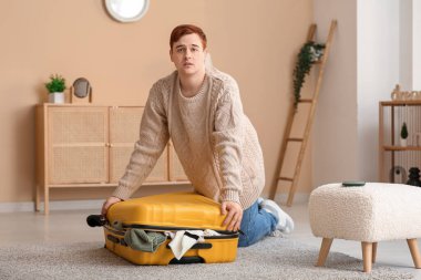 Evinde bavulu kapatmaya çalışan üzgün genç adam.