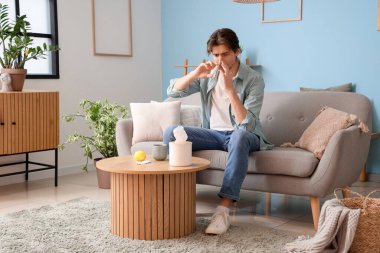 Hasta genç adam evdeki kanepede burun damlası kullanıyor.