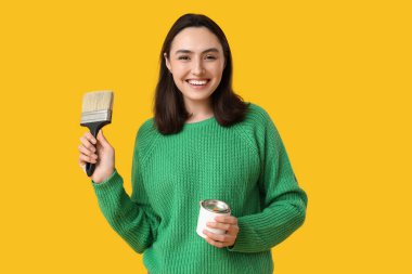 Sarı arka planda boya ve fırçayla genç bir kadın.