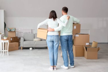 Taşındığı gün, arka manzaralı odada kutuları olan mutlu genç çift.