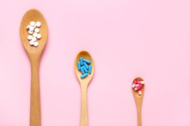 Ahşap kaşıklar ve pembe arka planda farklı haplar.