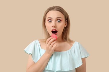 Güzel genç bir kadın bej arka planda tatlı badem kurabiyesi yiyor.