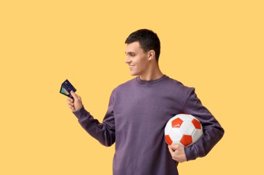 Sarı arka planda futbol topu ve kredi kartı olan genç bir adam.