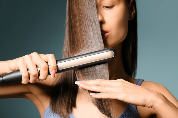 Красивая молодая женщина выпрямляет волосы на бирюзовом фоне, крупный план