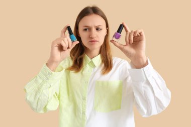 Bej arka planda oje şişeleri olan düşünceli genç bir kadın.