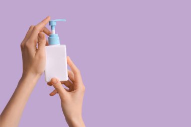 Leylak arka planına karşı doğal krem şişesi olan kadın elleri, yakın plan.