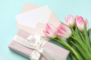 İçinde boş kart, hediye kutusu ve mavi arka planda pembe laleler olan zarf.