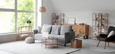 Gri kanepesi ve büyük penceresi olan aydınlık oturma odasının içinde.