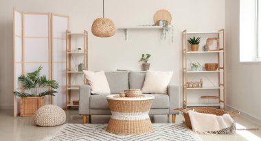 Yastıklı gri kanepe, hasır masa, açık oturma odasında puf ve sepet.