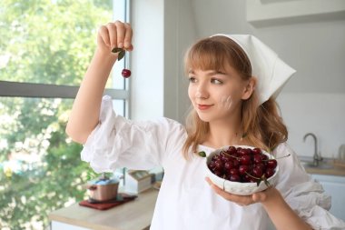 Mutfakta bir kase kirazla güzel, mutlu genç bir kadın.
