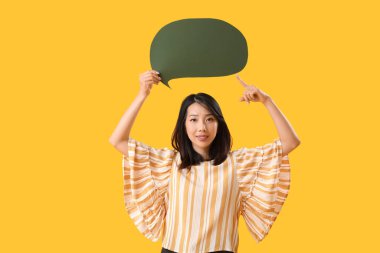 Güzel Asyalı kadın sarı arka plandaki boş konuşma balonunu işaret ediyor.