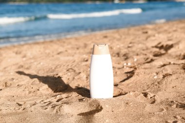 Kumsalda okyanus kıyısında kumda bir şişe güneş kremi.