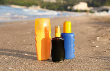 Kumsalda okyanus kenarında kumların üzerinde güneş kremi şişeleri.