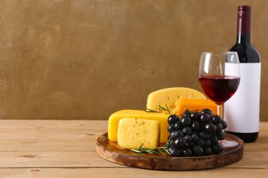 Kahverengi duvarın yanındaki masada lezzetli peynir, üzüm, şişe ve şarap tabağı.