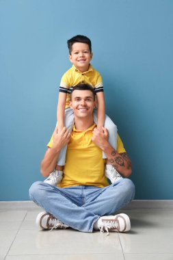 Mavi duvarın yanında küçük oğlu olan genç bir adam.