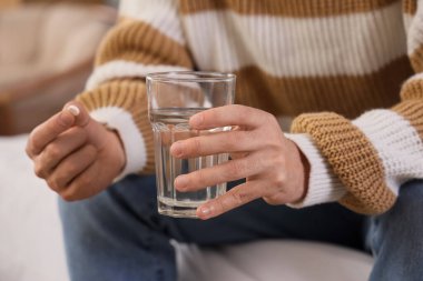 Yatak odasında elinde bir bardak su ve hap olan genç adam, yakın plan.