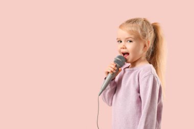 Küçük şirin kız pembe arka planda mikrofonla şarkı söylüyor.