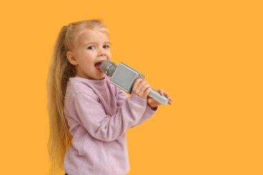 Sarı arka planda mikrofonla şarkı söyleyen sevimli küçük kız.