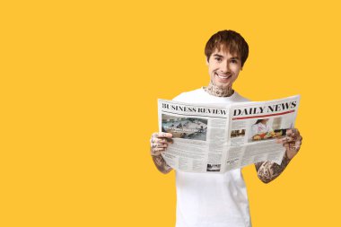 Sarı arka planda gazetesi olan yakışıklı bir genç.