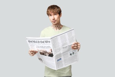 Gri arka planda gazetesi olan yakışıklı bir genç.