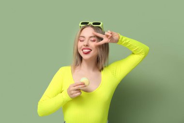 Sarı tatlı badem kurabiyeli güzel bir kadın yeşil arka planda zafer jesti sergiliyor.