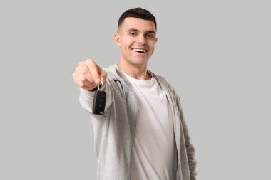 Gri arka planda araba anahtarı olan genç bir adam.