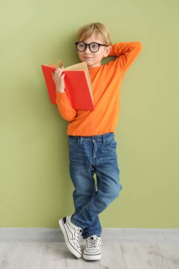 Gözlüklü şirin bir çocuk. Renk duvarına karşı duran açık bir kitabı var.