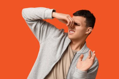 Turuncu arka plandaki kötü koku yüzünden burnunu çimdikleyen yakışıklı genç adam.