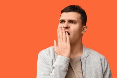 Yakışıklı genç adam turuncu arka planda kötü kokular alıyor.