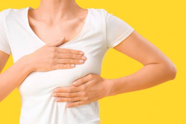 Sarı arka planda göğüslerini kontrol eden genç bir kadın, yakın plan. Kanser farkındalığı kavramı