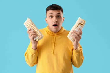 Şok olmuş genç bir adam mavi arka planda lezzetli bir donör kebabıyla